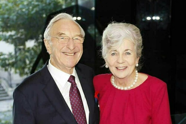 Martin Naughton is to the left in a dark suit and patterned tie, smiling next to Carmel Naughton on the right who is wearing a red dress and pearl necklace.