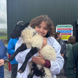 A smiling person holds a black and white lamb.