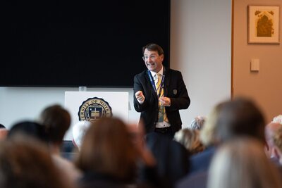 Man in a suit with a Notre Dame lanyard speaks at a podium with the University seal.